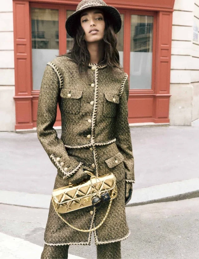 Model in gold-and-brown Chanel tweed coat and hat carrying a gold quilted chain bag on a Paris street