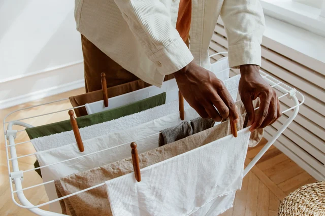 Hands hanging washing on an indoor drying rack, with an air gap left between the pieces