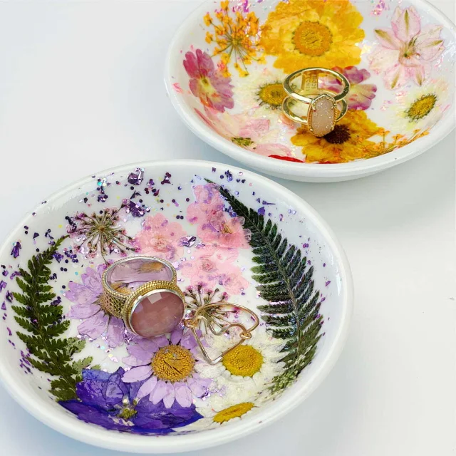 Two pressed flower resin ring dishes with real dried botanicals and gold jewelry, glossy epoxy finish