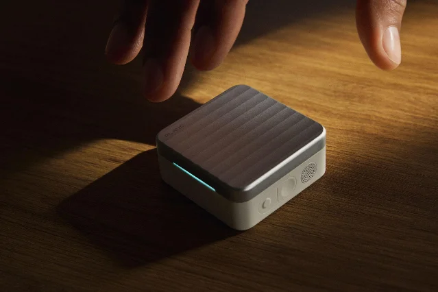 Plaud One charging case on a wooden table with a hand hovering above it