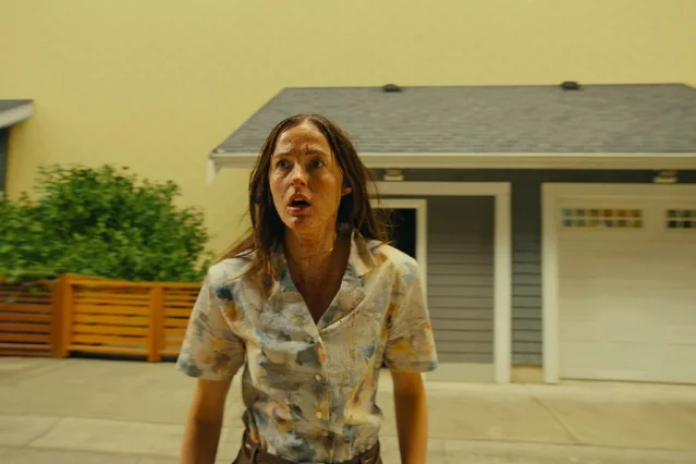 Renate Reinsve standing on a suburban driveway with her face streaked with dirt in Backrooms