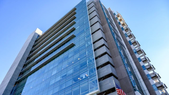 Modern glass office building under a clear blue sky with a US flag visible — US financial sector backdrop
