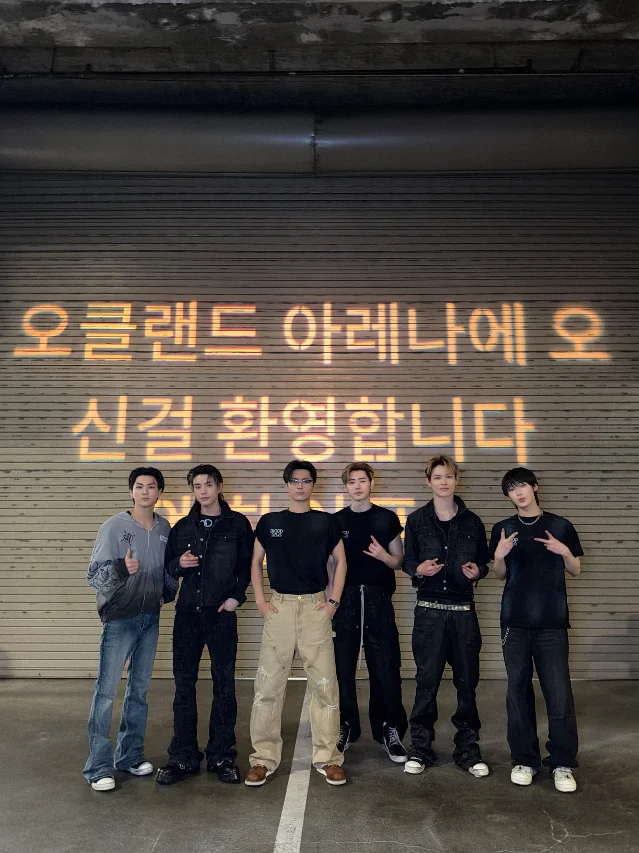 ENHYPEN members pose beneath an Oakland Arena welcome message