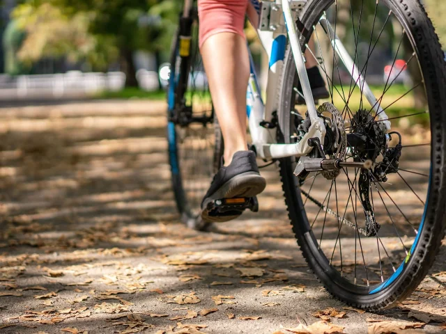 Close-up of bicycle pedaling through autumn leaves, focusing on foot and drivetrain