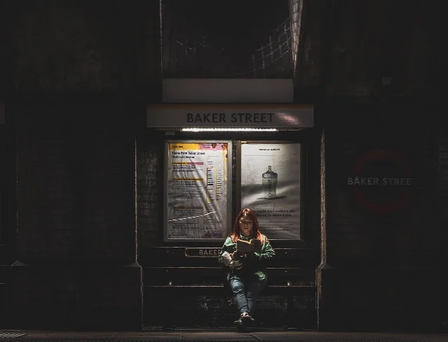 A commuter seated at a railway station reading a book while waiting for a train
