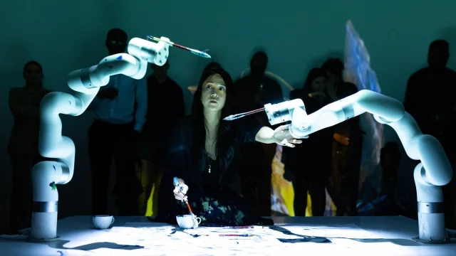 Sougwen Chung working with two robotic arms during a live drawing performance