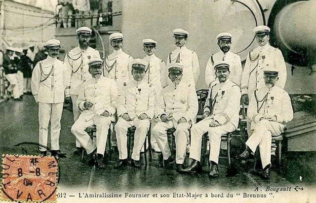 A sepia postcard photograph of eleven French naval officers in white summer uniforms, five seated and six standing, on a ship's deck