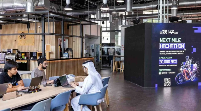 Students work beside the Next Mile Hackathon event poster at 42 Abu Dhabi