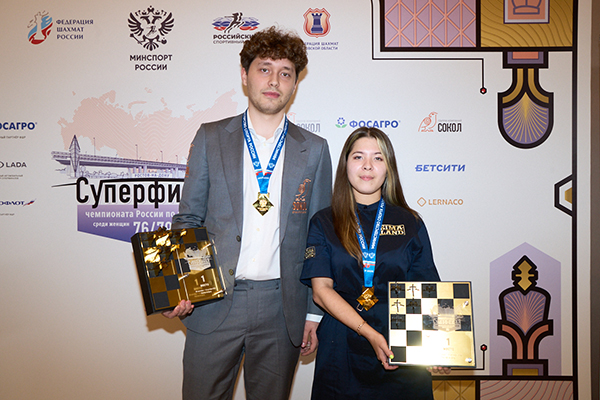 Andrey Esipenko and Leya Garifullina standing together with medals and trophies against a sponsor backdrop