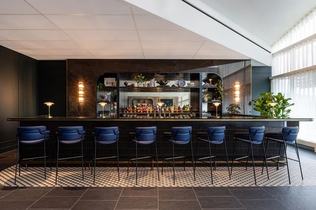Interior of the new Centurion Lounge at Amsterdam Airport Schiphol, with a mirrored bar, blue leather bar stools and a blue-and-white tiled floor