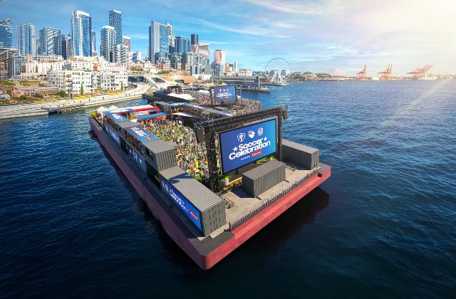 Floating waterfront soccer celebration setup at Pier 62 with screens and Elliott Bay behind it.