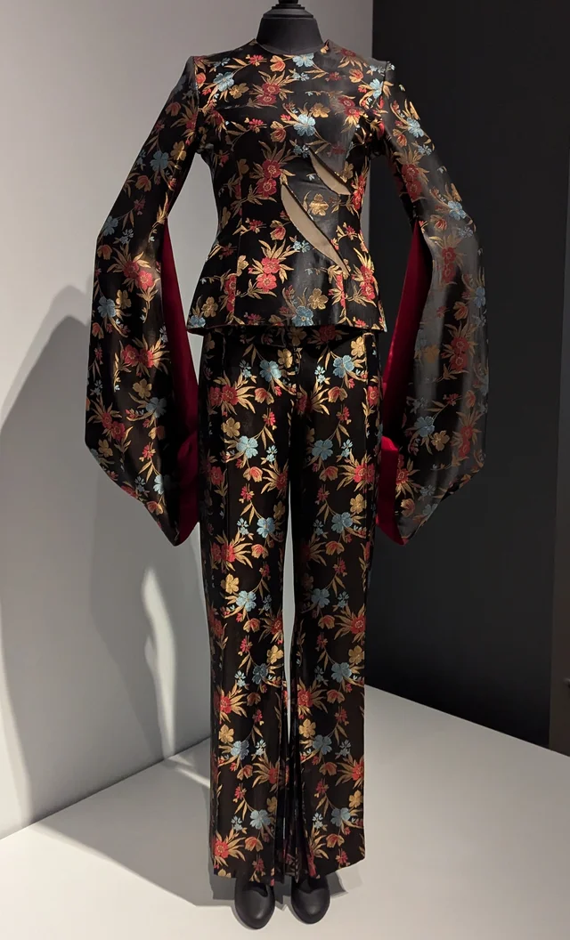 A floral brocade top with wide kimono sleeves and a slash across the front, on a mannequin, with matching trousers