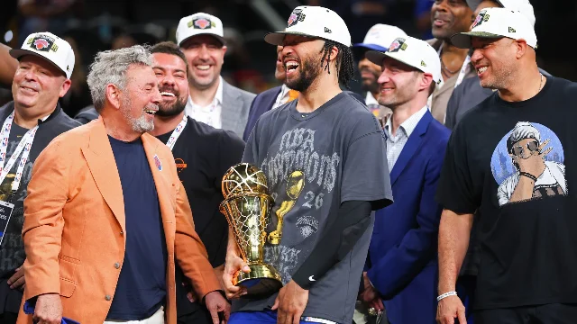 Jalen Brunson holds the Larry O'Brien Trophy, laughing alongside James Dolan after the Knicks win the 2026 NBA championship