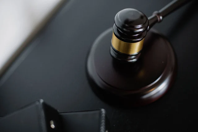 Wooden judge's gavel resting on a round surface beside legal folders in a courtroom