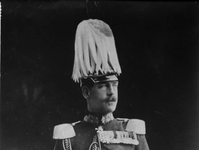 A moustached man in a plumed helmet and braided dress uniform with epaulettes, facing right