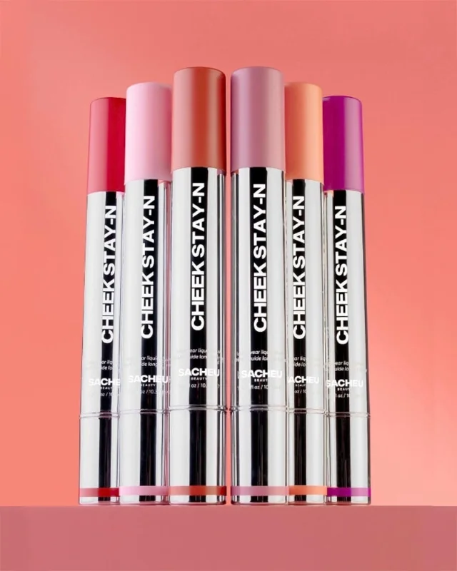 Six SACHEU Cheek STAY-N liquid blush tubes fanned out against a warm peach background — shades range from soft pink to deep pink berry