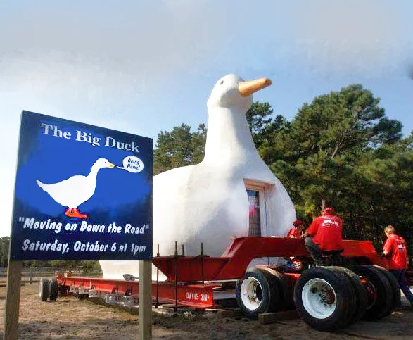 The Big Duck on a trailer during its 1988 relocation, with a sign advertising "Moving on Down the Road".