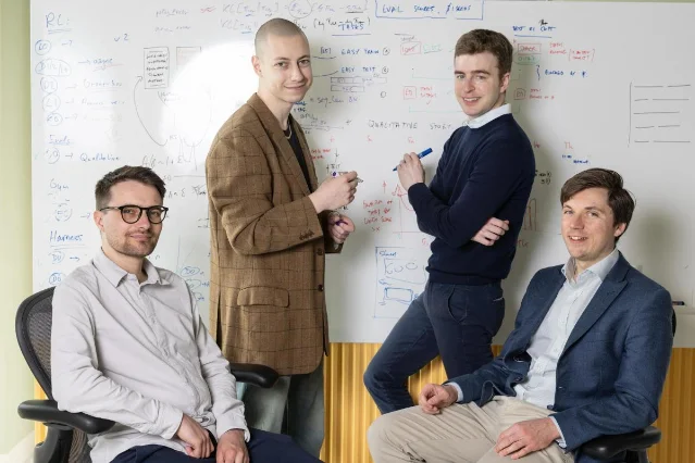 Four Inherent cofounders standing and sitting in front of a whiteboard covered with research notes and formulas