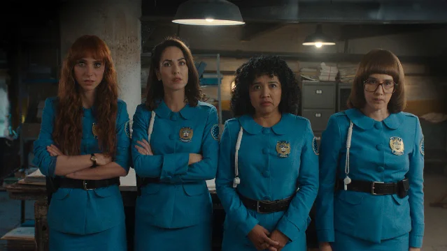 Four women in blue police uniforms stand together in a dim interior.