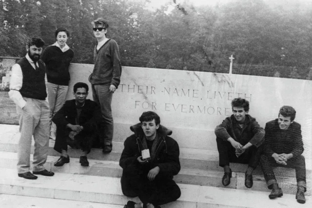 a black-and-white photograph of seven young people posed on the steps of a stone war memorial, one seated in the middle in a dark jacket and bow tie