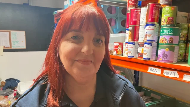 Jill McBurney standing in front of orange shelves stacked with canned pet food at the USPCA centre in Newry.