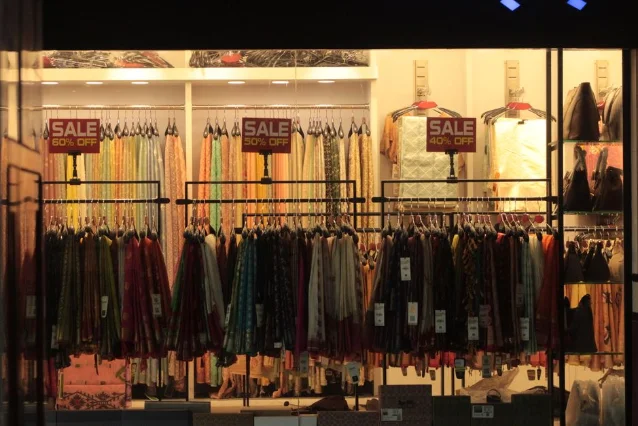 Clothing store interior showing three clothing racks with red sale signs reading "60% OFF," "50% OFF," and "40% OFF" in a lit boutique