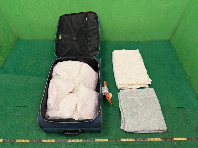 Open blue hard-shell suitcase on a green floor, packed with large white plastic bags of suspected ketamine — the 16 kg seizure from the Japanese passenger's checked baggage, HKIA, June 17, 2026
