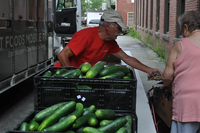 A volunteer hands fresh produce to a guest beside a Good Shepherd Food Bank Food Mobile truck.