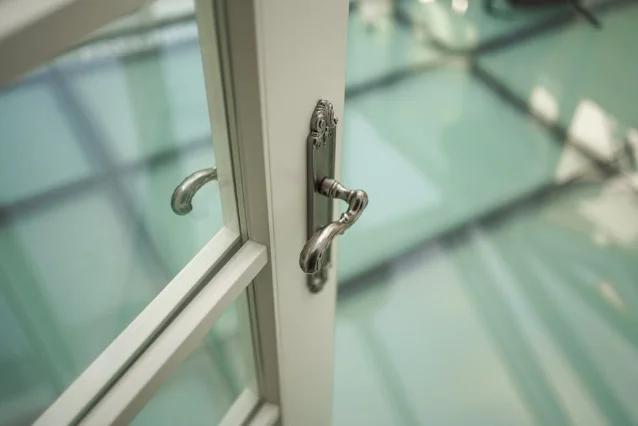 Ornate door handle on a white aluminium-framed casement door, showing hardware finish and mounting style