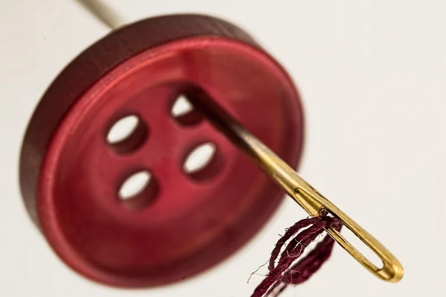A needle and thread passing through a red four-hole button