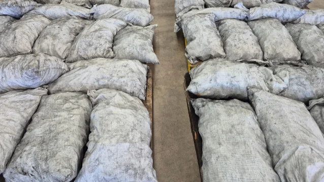 Rows of grey-white burlap sacks arranged on pallets inside a warehouse aisle — the charcoal bags in which 320 kg of methamphetamine was concealed