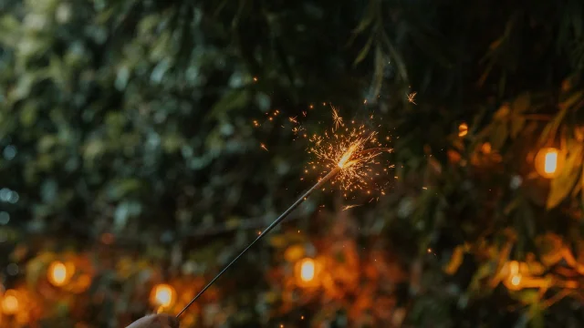 A lit sparkler held at arm’s length at night