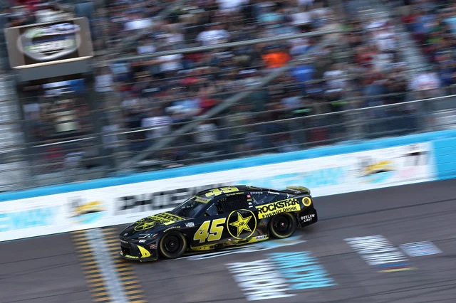 A black No. 45 Rockstar Energy Drink Toyota NASCAR Cup car at speed on a track, the grandstand crowd blurred behind it