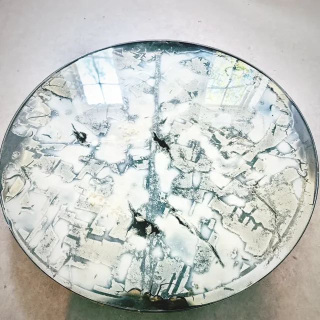 A circular table surface showing a cracked, map-like white growth pattern under glass