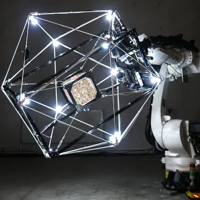 A white industrial robot arm holding a glowing geometric frame with a square fungal growth chamber inside