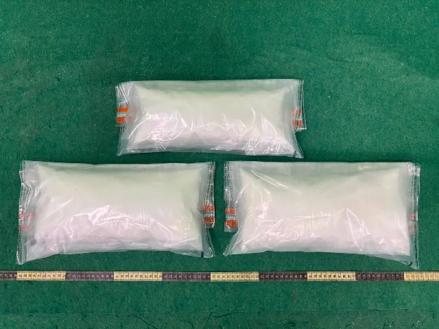 Three translucent vacuum-sealed bags of white crystalline powder arranged in a triangle on a green inspection floor, with a measuring tape along the bottom edge — the 4 kg ketamine seizure from Case 3
