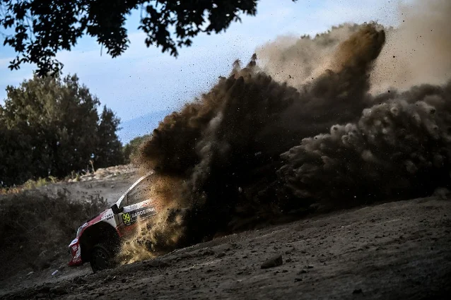 A rally car throwing up a huge plume of dust on a Sardinian gravel stage