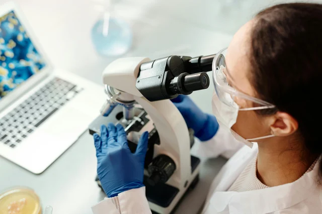 Scientist in protective lab gear examining samples under a microscope — representing flu and H5N1 laboratory surveillance