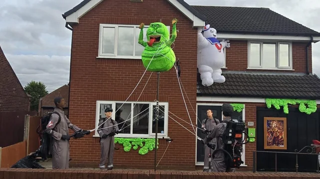 a red-brick house with four figures in khaki flight suits on the lawn and large green and white figures fixed to the walls