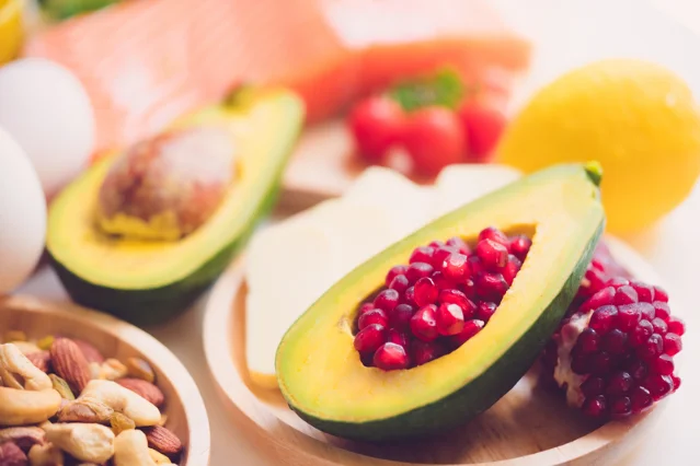 Avocado, pomegranate seeds, mixed nuts, eggs, salmon, tomatoes and citrus arranged on a wooden surface — representing the variety of foods associated with communal dining in older adults