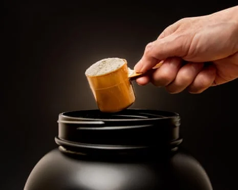 Close-up photograph of a scoop of whey protein powder being held above a container