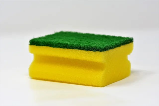 A yellow and green household sponge on a white background