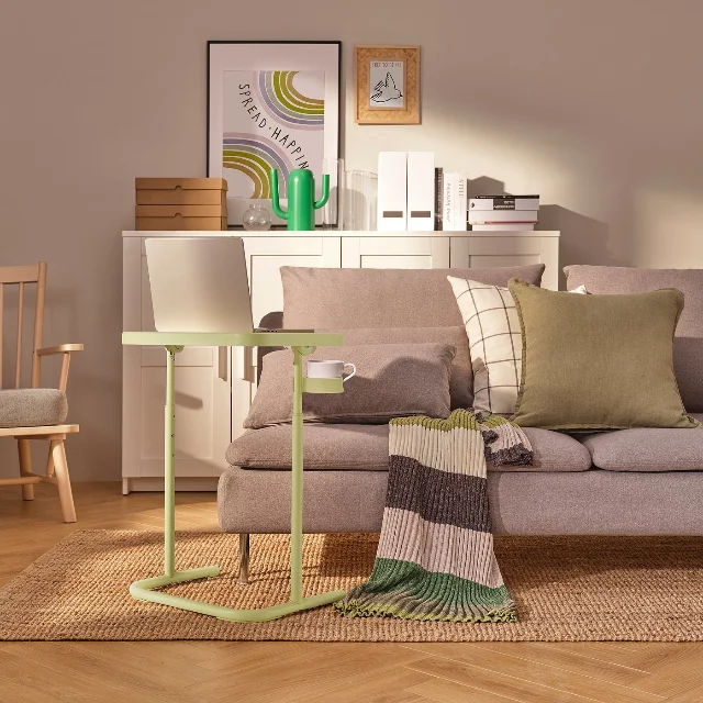 BJÖRKÅSEN laptop stand in yellow-green beside a grey sofa in a styled living room