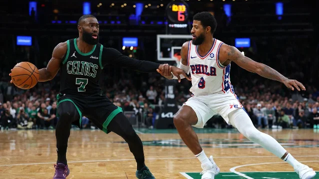 Jaylen Brown in Celtics green defends Philadelphia 76ers forward Paul George in white during an NBA game.