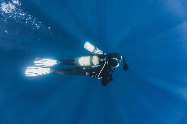 A scuba diver swimming underwater with an oxygen cylinder, viewed from above