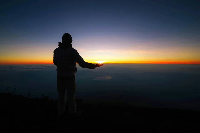 Hiker standing at the summit of Mount Fuji against an orange sunrise sky
