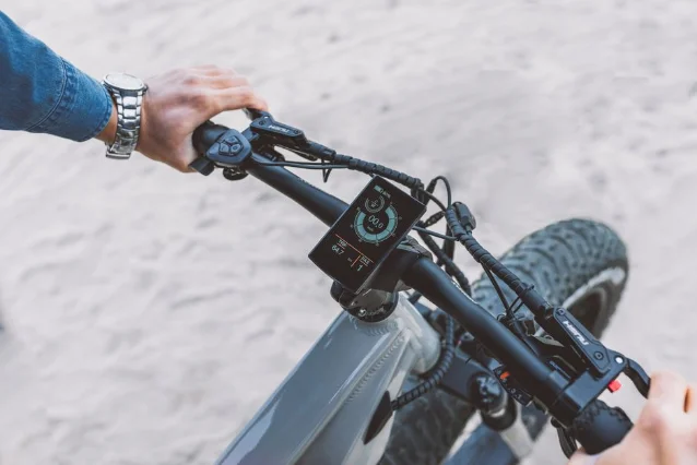 First-person rider view of eBike handlebar with touchscreen display showing speed, battery, and assist-level tiles