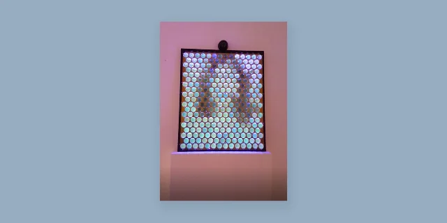 Living Mirror gallery installation showing illuminated circular optical cells mounted in a dark enclosure