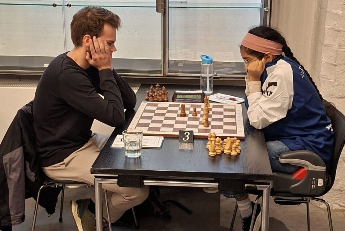 Bodhana Sivanandan, wearing a headband, playing a male opponent across a club chess table