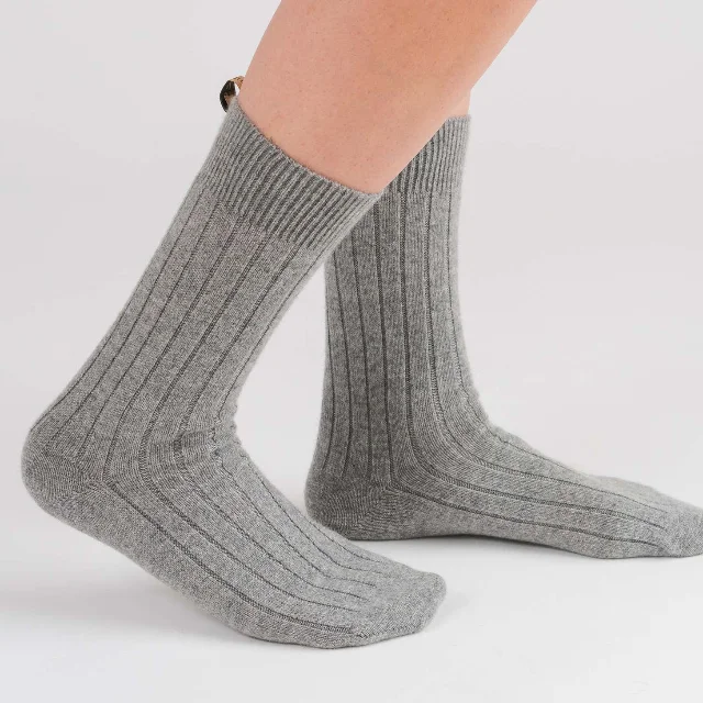 A pair of Comme Si cashmere socks in heather gray, shown on a person's lower legs
